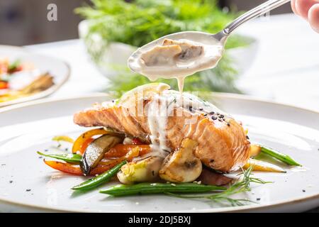 Gegrillter Lachs mit Gemüse und Pilzsauce auf einem Teller darüber gegossen. Stockfoto