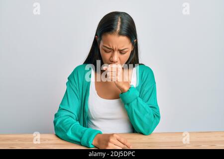 Schöne hispanische Frau trägt Freizeitkleidung auf dem Tisch sitzen Gefühl unwohl und Husten als Symptom für Kälte oder Bronchitis. Health care concep Stockfoto