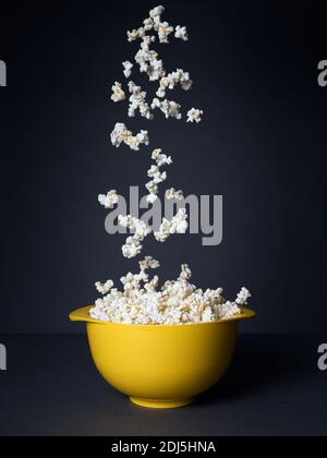 Popcorn fällt in eine gelbe Schüssel auf schwarzem Hintergrund Stockfoto