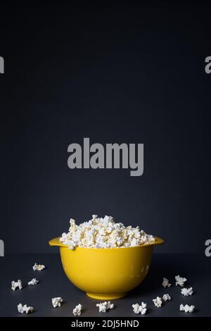 Popcorn in einer gelben Schüssel. Popcorn auf dunklem Boden verstreut Stockfoto