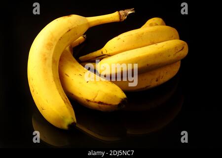 Bananen mit einigen dunklen Flecken mit Schatten isoliert auf schwarzem Hintergrund. Stockfoto