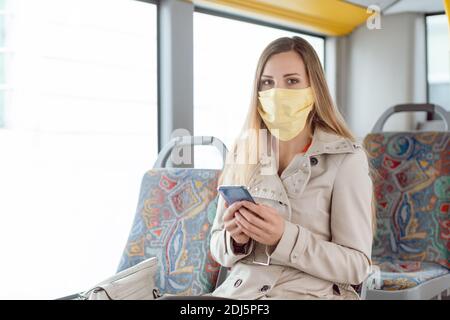 Frau, die im Bus Telefon benutzt und eine Gesichtsmaske trägt Stockfoto