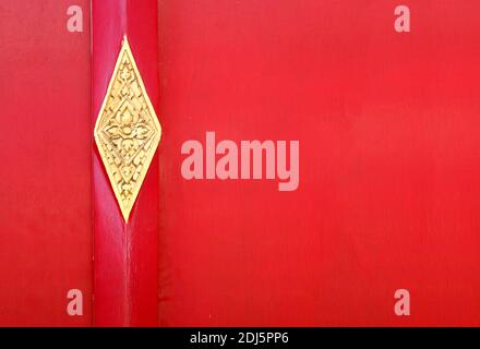 Rote Tür mit metallischem Element im asiatischen Stil. Rotes Holztor mit goldenen Details. Tür mit thai Blumenschmuck. Stockfoto
