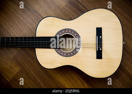 Die klassische Gitarre liegt horizontal auf dem Holzboden. Die klassische Gitarre steht auf dem Holzhintergrund.Rustikale Atmosphäre. Stockfoto