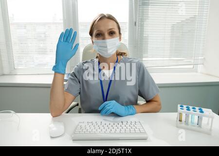 Junge weibliche Klinikerin oder Arbeiter des medizinischen Labors in Schutz arbeitskleidung zeigt ihre offene Handfläche für Sie, während Ellbogen zu halten Auf dem Tisch Stockfoto