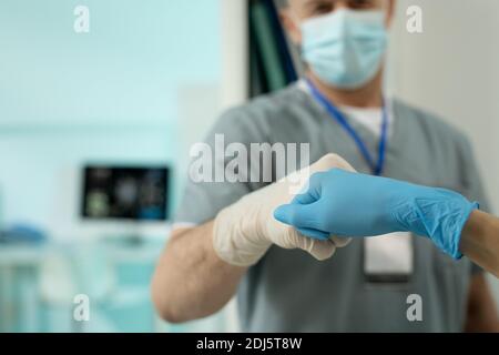 Handschuhen von zwei modernen Klinikern in der Herstellung von Schutzkleidung Punch Bump, während Begrüßung einander in der Arztpraxis Stockfoto