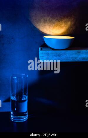 Stillleben einer Bambusschale gefüllt mit Licht auf einem Regal und einer Glasvase gefüllt mit Wasser auf einem Schreibtisch in der Nacht. Stockfoto