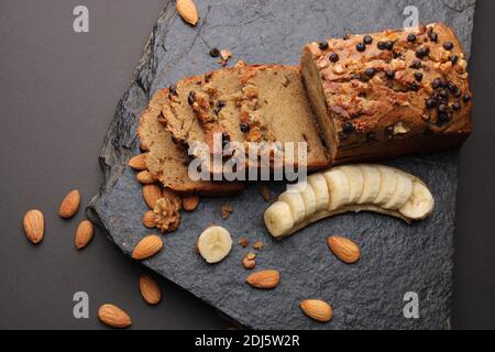 Laib Bananenbrot auf dunklem Stein Hintergrund. Mit Mandeln und Walnuss Stockfoto