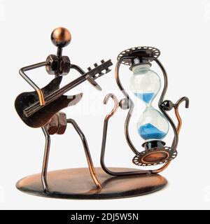 Sanduhr in einem Metallgehäuse und blauem Sand. Neben der Figur eines Mannes mit Gitarre. Isoliert auf weißem Hintergrund Stockfoto