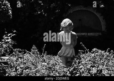 Eine Graustufenaufnahme einer Kinderstatue im Garten Stockfoto