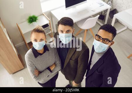 Gruppe von Mitarbeitern in Unternehmen in Gesichtsmasken im Büro stehen Und Blick auf die Kamera Stockfoto