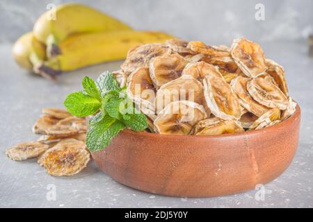 Hausgemachte getrocknete Banane, Bio-Bananenchips in Holzschüssel, auf grauem Beton-Tischhintergrund mit frischen gelben Bananen kopieren Platz Stockfoto