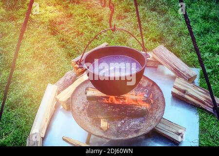 Brühe mit Fleisch wird in einem Retro-Topf auf dem Feuer gekocht. Kochen Essen an einem Sommerabend in der Natur Stockfoto