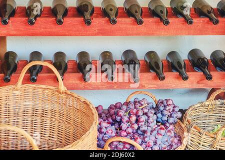 Professionelle Weinherstellung in Europa. Korb mit roten und weißen Trauben und Weinflaschen auf den Regalen. Stockfoto