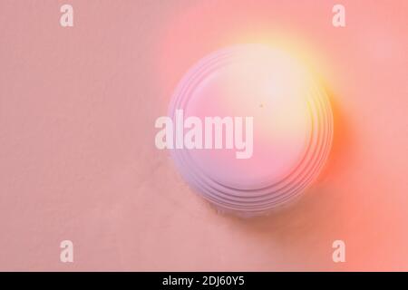 Rauchmelder mit weißem Rauch und roter Warnleuchte. Sensor an der beigefarbenen Decke. Rauchbrandalarm im aktiven Zustand, Hintergrund der Wand. Stockfoto