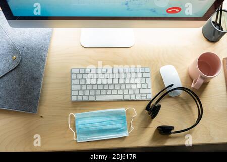 Überblick über den Arbeitsplatz eines modernen Kundendienstmitarbeiters mit Computermonitor, Tastatur, Maus, Headset, Tasse, Maske und Bleistiften Stockfoto