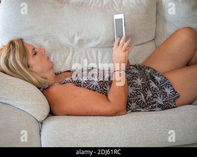 Erkennbare reife Frau, die auf dem Sofa mit Tablet in den Händen liegt Stockfoto