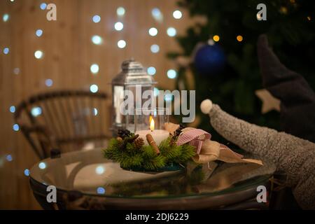 Stimmungsvolles weihnachtliches Interieur mit brennender Kerze auf dem Tisch In einem schönen Kerzenhalter aus Fichte mit einem Bokeh aus einer Girlande in der Stockfoto