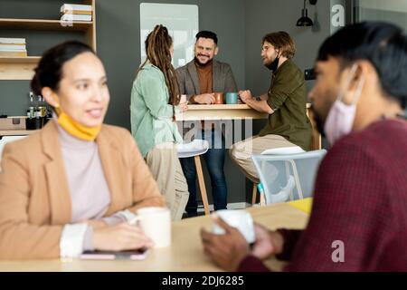 Gruppe von interkulturellen glücklich Büroangestellten in Casualwear Blick auf Einander beim Kaffee trinken und Arbeitspläne besprechen Pause Stockfoto