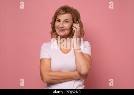 Glückliche fröhliche Frau, die mit einem Freund auf dem Handy spricht, lacht. Studio auf rosa Wand aufgenommen Stockfoto