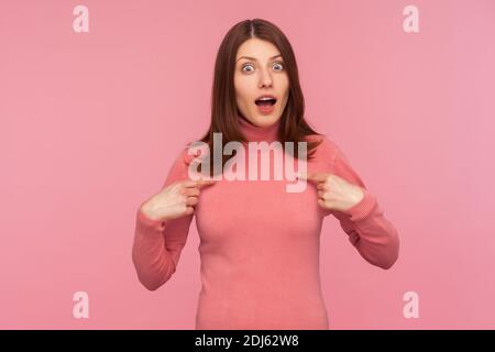 Unsichere schockierte Frau mit braunen Haaren in rosa Pullover zeigt Finger auf sich selbst, überrascht mit ihrer Teilnahme, kann nicht an plötzlichen Sieg glauben. Stockfoto