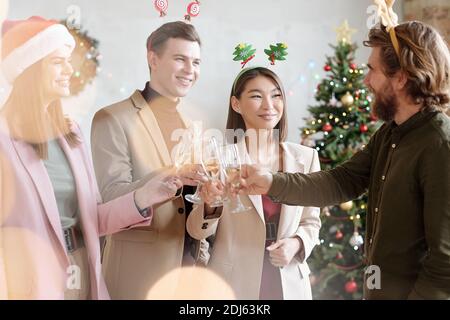 Fröhliche junge Kollegen in Weihnachten Stirnbänder mit Flöten von klirren Champagner während der Weihnachtsfeier Stockfoto