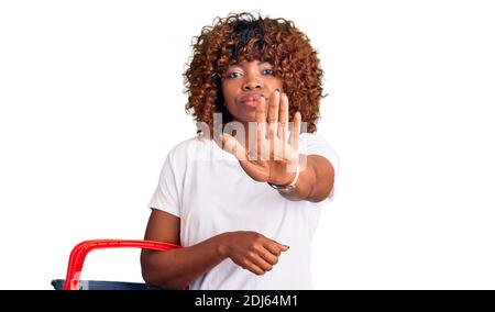 Junge afroamerikanische Frau hält Supermarkt Warenkorb mit offener Hand tun Stop-Zeichen mit seriösen und selbstbewussten Ausdruck, Verteidigung Geste Stockfoto