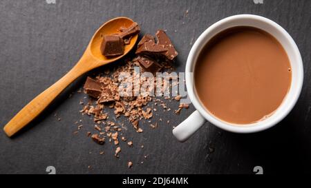 Flaches Lay von einem Schokoladenmilchgetränk mit einem Holzlöffel und zerbröckelter Schokolade auf der Seite präsentiert. Stockfoto