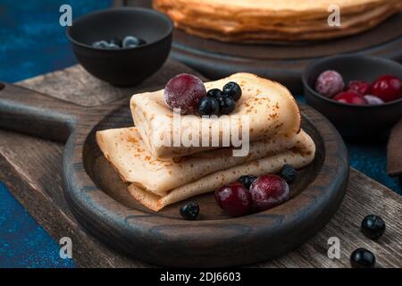 Gefrorene Kirschen und Rowan mit Pfannkuchen auf einem Holzteller auf blauem Hintergrund. Stockfoto