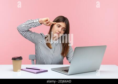 Deprimiert unglücklich Frau Büroangestellte in gestreiften Hemd sitzenden Arbeitsplatz zeigt dumme Geste Laptop-Display im Gespräch auf Videoanruf. Studio im Innenbereich Stockfoto