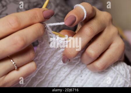 Die Frau strickt. Holzstricknadeln und weiße Fäden. Nahaufnahme. Stockfoto