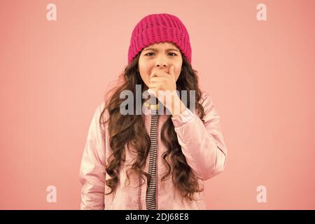 Kleine Mädchen fangen Husten. In diesem Winter keine Grippe. Tragen Sie warme Kleidung in der kalten Jahreszeit. Winterferienaktivität. Kleiner pinkfarbener Hintergrund. Modischer Stil für Kinder. Strickmütze und Puffer-Mantel. Wintergrippe. Stockfoto