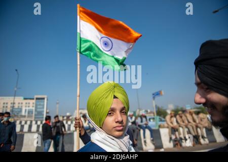 Ein Sikh-Junge steht während der Demonstration in der Nähe einer indischen Nationalflagge.die Proteste der Bauern an der Grenze zwischen Delhi und Uttar Pradesh dauern an. Morgen werden die Bauernführer eines Tages in einen Hungerstreik treten. Tausende Bauern protestieren an verschiedenen Grenzpunkten von Delhi und fordern die Abschaffung neuer Agrargesetze. Stockfoto