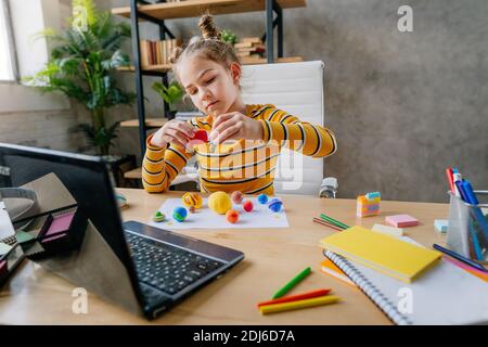 Kleine 8 Jahre altes Mädchen mit Laptop, um online Planeten des Sonnensystems am Schreibtisch im Zimmer zu studieren. Junge weibliche Grundschülerin w Stockfoto