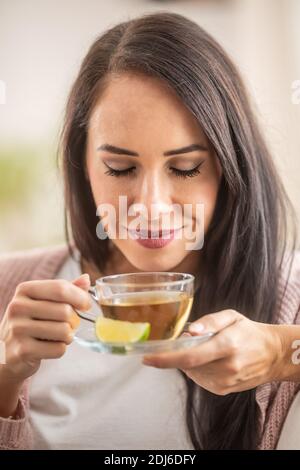Gut aussehende Frau genießt den Geruch eines frisch gebrühten Tees mit geschlossenen Augen. Stockfoto