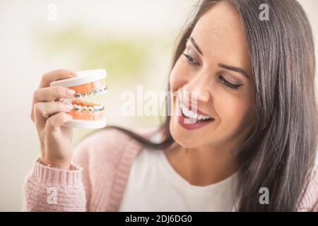 Lächelndes Weibchen schaut auf die bunten Zahnspangen an der Zahnsprothese in ihrer Hand. Stockfoto