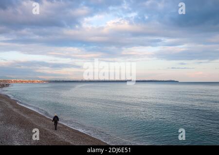 Fischer zu Fuß am Strand von Antalya Taurus Berge und Rosa lila wolkigen Himmel im Hintergrund Stockfoto