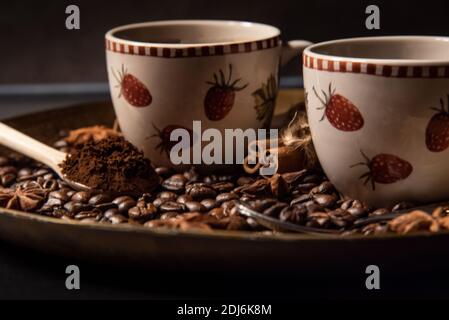 Zwei Tassen Kaffee auf einem goldenen Serviertablett, umgeben von gerösteten Kaffeebohnen, gemahlenem Kaffee und Gewürzen. Stockfoto