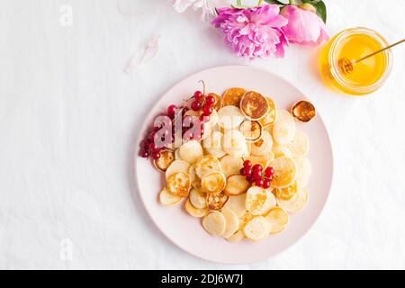 Kleine Pfannkuchen mit Beeren, Honig, Blumen. Pfannkuchen, Müsli. Das Konzept des Frühstücks, Essenstrends. Speicherplatz kopieren. Stockfoto