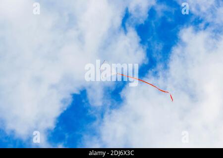 Weiß rot Schwanz Drachen fliegen gegen blauen Himmel mit gefleckt Wolken Stockfoto