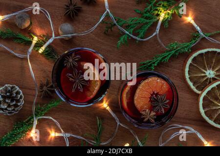 Zwei Gläser Glühwein mit Zitrusfrüchten, Sternanis, Muskatnuss auf Holztisch. Saisonales Weihnachtsgrüllgetränk, Neujahrsdekorationen und Lichter, t Stockfoto