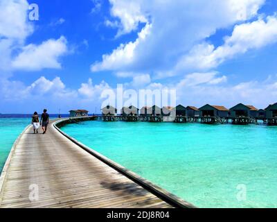 Ein Paar, das auf einem Pier in einem wunderschönen Resort läuft Mit Holzhütten auf dem klaren Wasser der Malediven gebaut Stockfoto