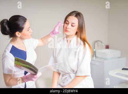 Junge hübsche Frau kam in einen Schönheitssalon und berät mit einer Kosmetikerin zu Anti-Aging-Behandlungen. Stockfoto