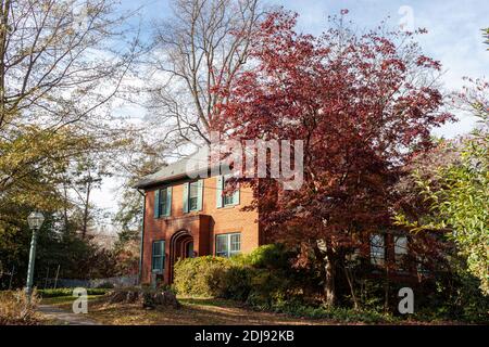 Rockville, MD, USA 11/20/2020: Ein zweistöckiges Ziegelhaus mit grünen Fensterläden und einer Bogentür. Dieses historische Haus befindet sich in einem ruhigen Garten mit Stockfoto