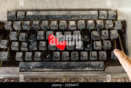 Alte Schreibmaschine mit speziellen Knöpfen, LIEBESWORT und Hand des Mannes drücken Sie hinein Stockfoto