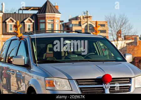 Frederick, MD, USA 12-02-2020: Ziergeweih an Fenstern und ein roter Nasendekor an der Vorderseite eines Autos. Eine schöne weihnachts-Kombination macht die Stockfoto
