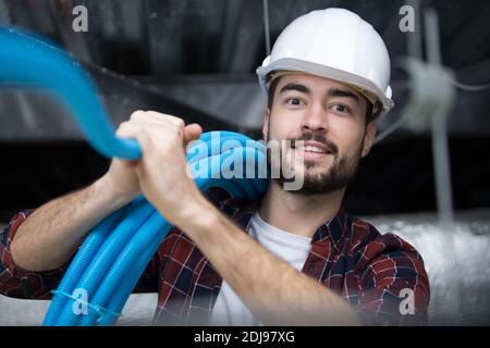 Männlicher Auftragnehmer, der blaue Rohre im Dachraum installiert Stockfoto