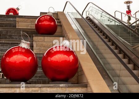 Sehr große rote glänzende dekorative Kugeln, werden von der Rolltreppe in einem Einkaufszentrum platziert. Diese Ornamente sind Vorbereitung für die Weihnachtszeit. Ein Ribbo Stockfoto