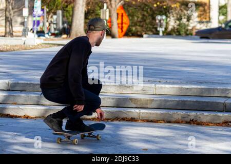 Ein junger Kaukasusmann mit Hut, Canvas-Hosen und Sneakers hockt auf seinem Skateboard, bevor er über die Treppe in die Luft springt Stockfoto