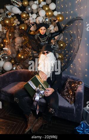 DJ Santa Claus mit Sonnenbrillen und Kopfhörer Hören zu Weihnachten Musik und Snow Maiden Schwarz Lederjacke Spaß haben. Rockparty Time. Emotionales Porträt in voller Länge Stockfoto